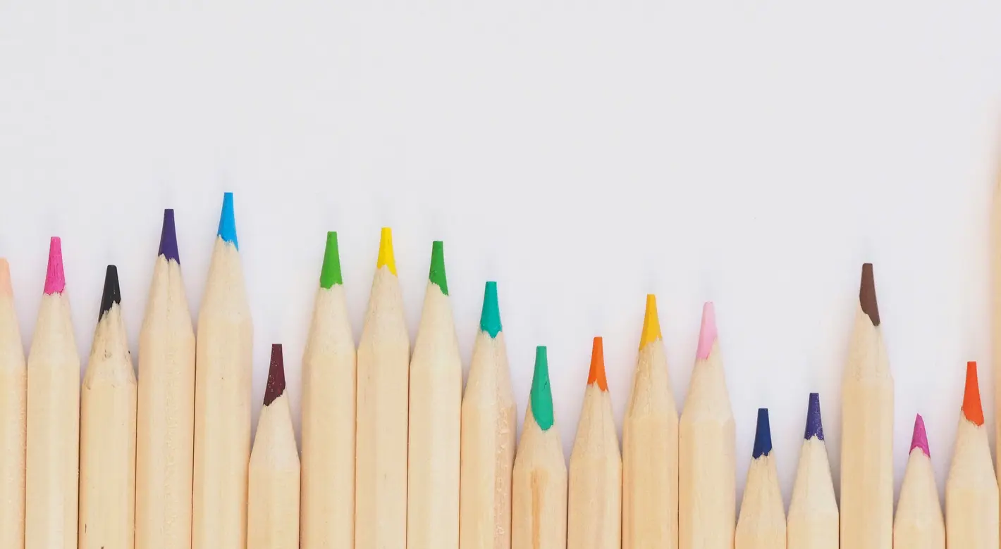 A row of sharpened colored pencils lines the bottom edge of a white background, leaving blank space above.