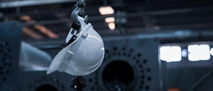 White safety helmet hanging in an industrial setting, representing HSE and quality standards