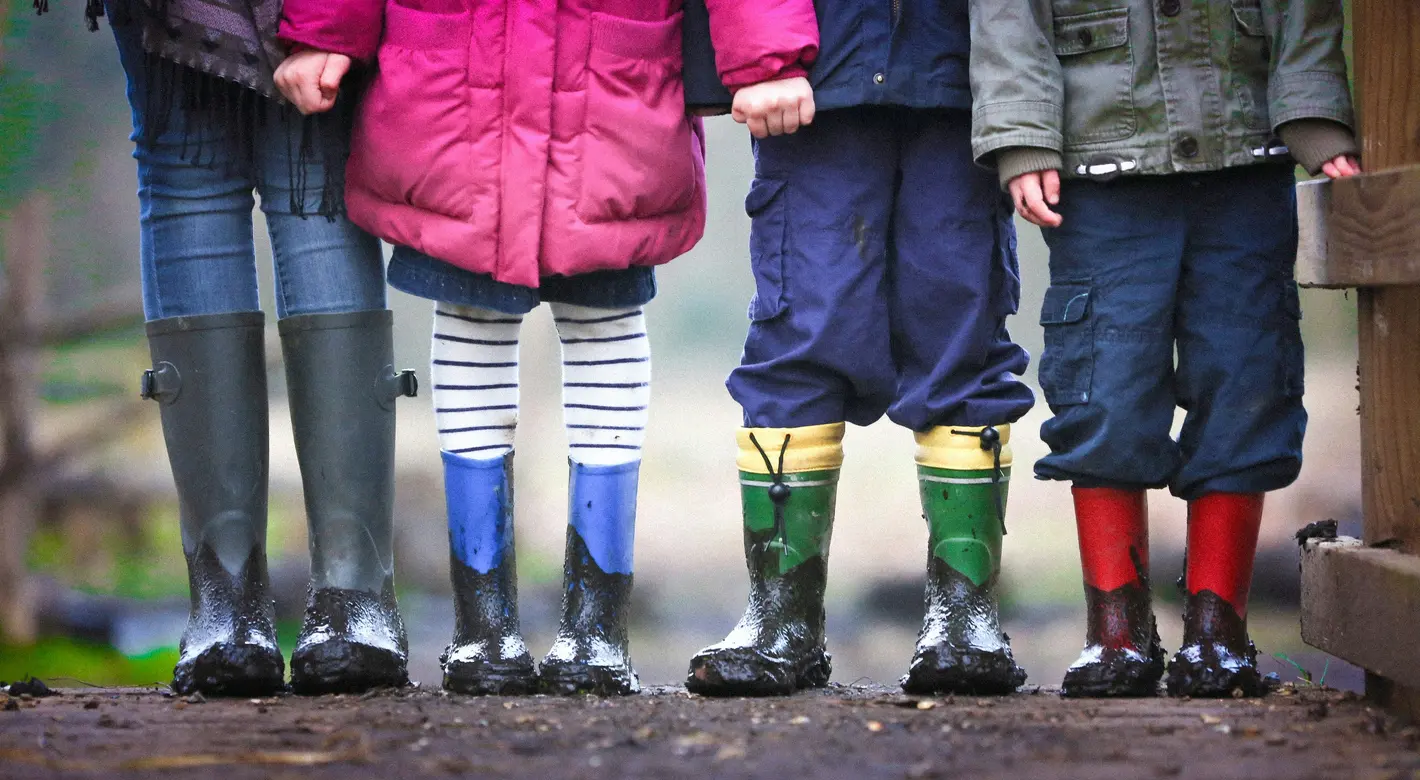 Close-up of an adult and three children standing in muddy wellington boots, showing only their legs and coats.
