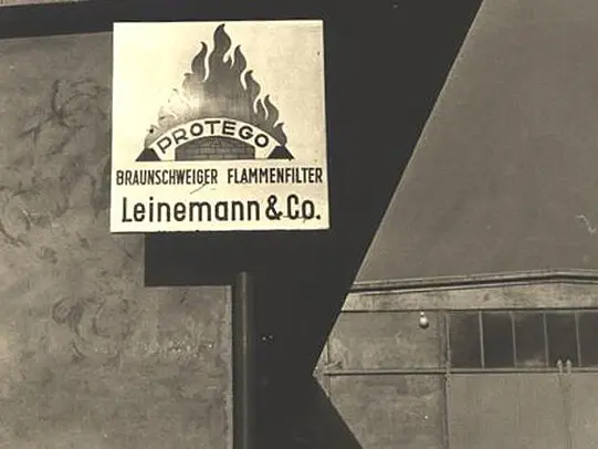 Close-up of a vintage Protego sign reading “Braunschweiger Flammenfilter Leinemann & Co.” with a flame logo mounted on an industrial wall.