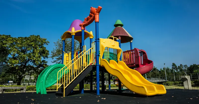Unter strahlend blauem Himmel steht ein farbenfroher Spielplatz mit Rutschen und Kletterplattformen.