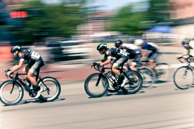 Un peloton de cyclistes sur route file à toute allure, avec un effet de flou de mouvement prononcé, soulignant la vitesse dans une rue de la ville.