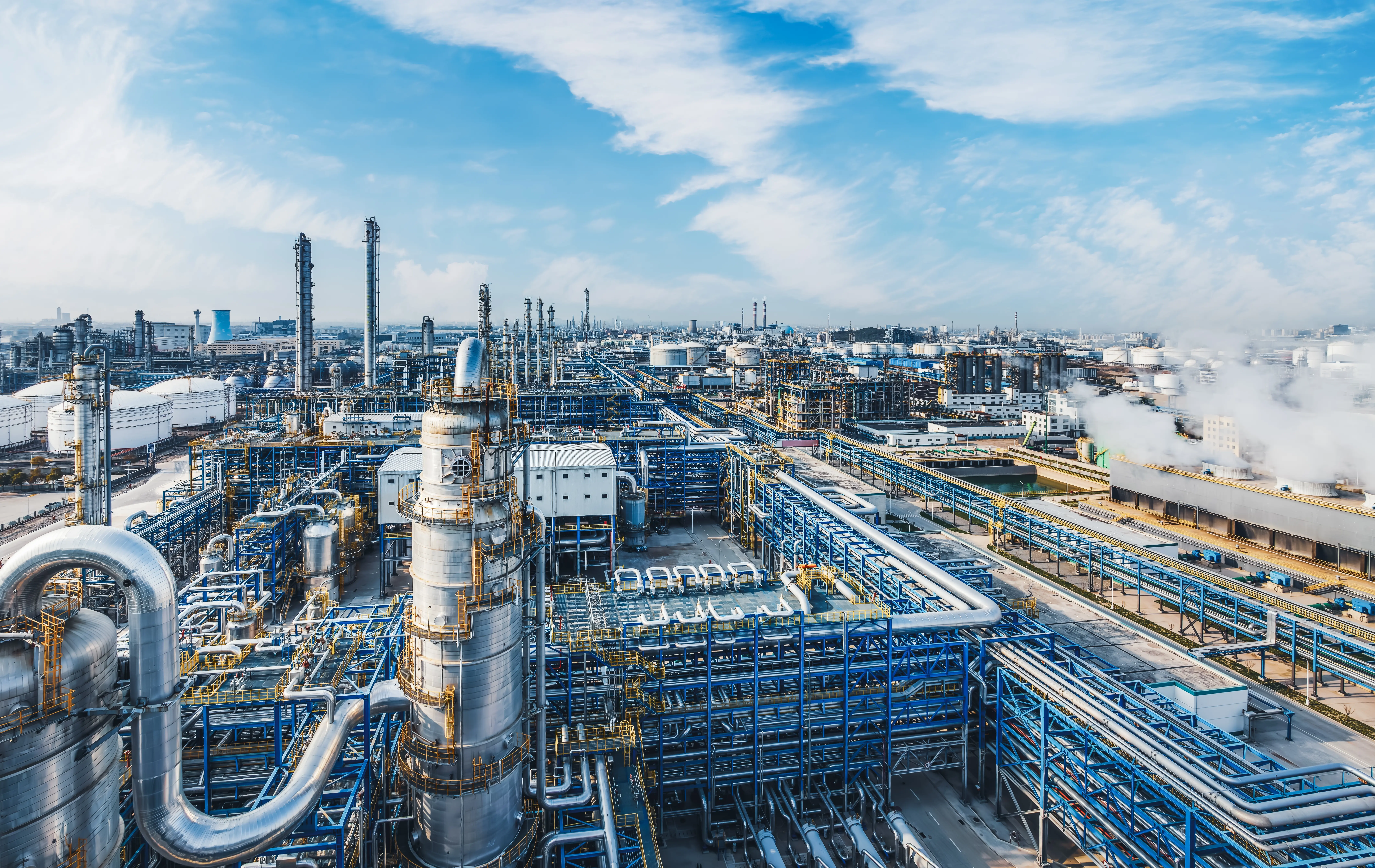 Des réservoirs de stockage d'émissions industrielles et de gaz de torchère sous un ciel bleu, dont la surface métallique se reflète