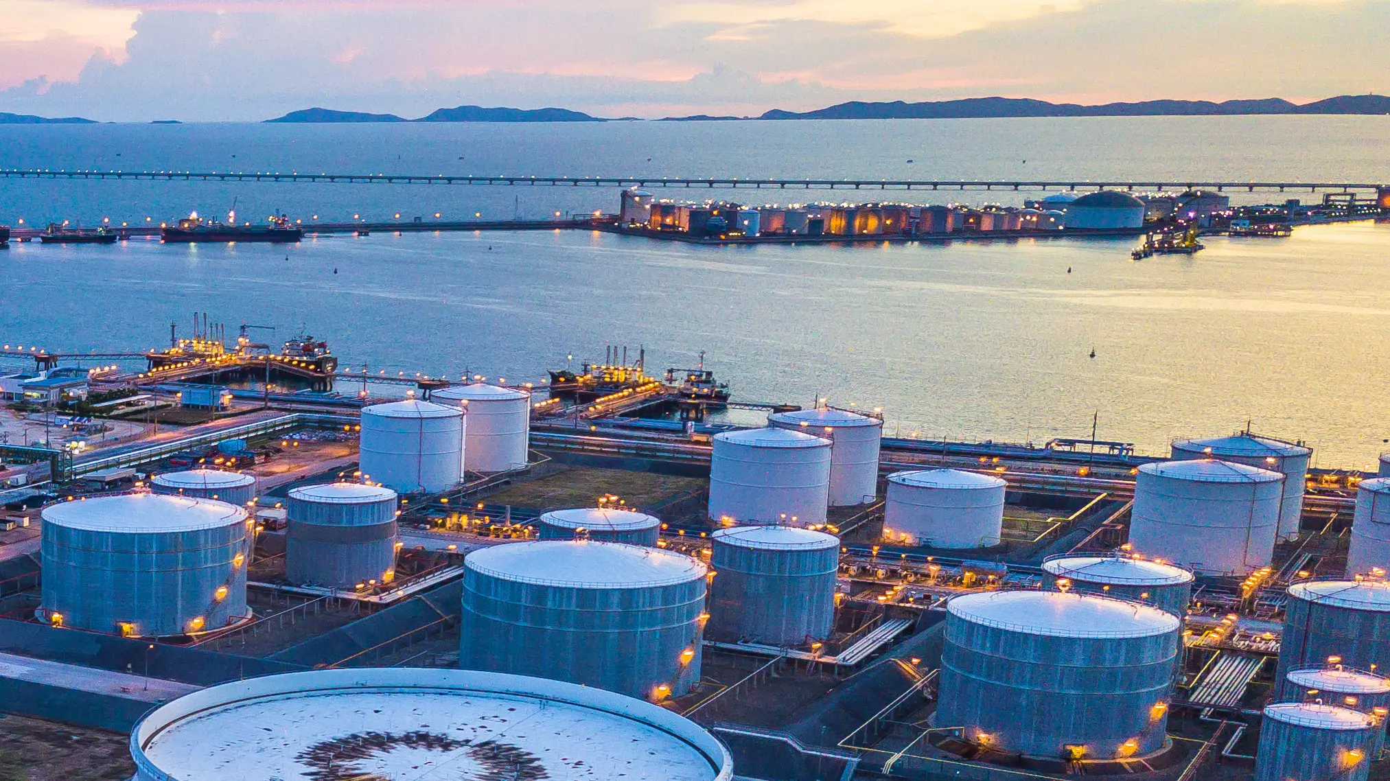 Un complexe industriel pétrolier et gazier doté de grands réservoirs de stockage, situé près d'un port, au crépuscule