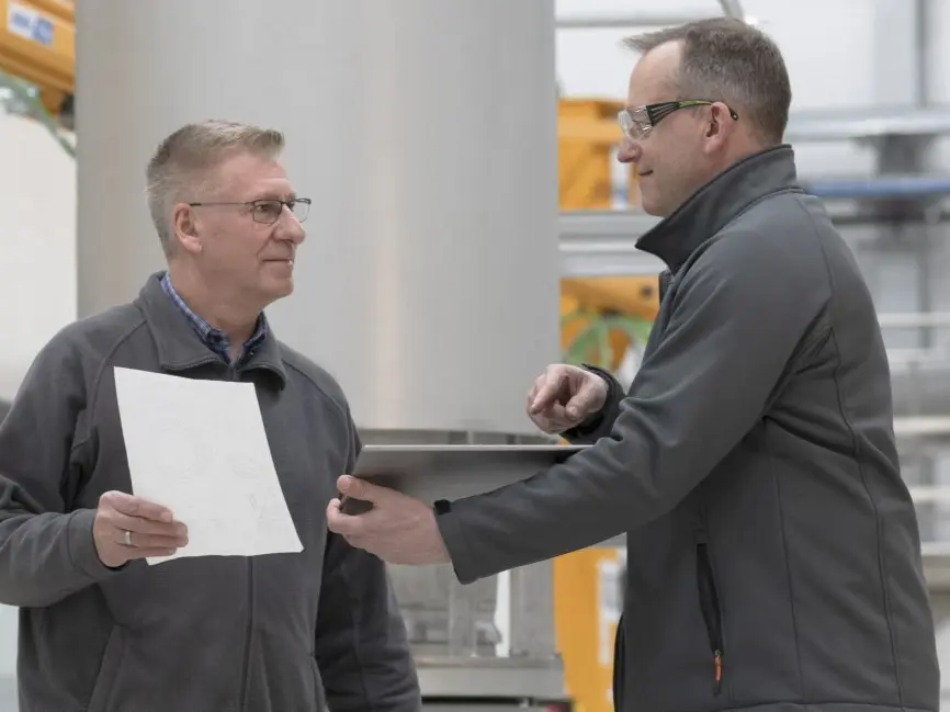 A supervisor discussing a document with an employee in an industrial setting, promoting compliance, respect, and tolerance